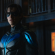 A front-lit Nightwing stand imposingly in a dark alley, an intense look on his face.